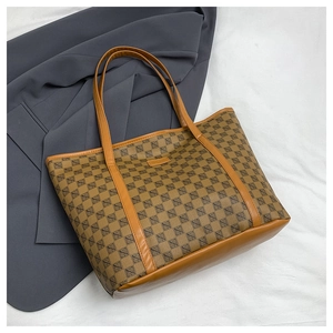 Detailed view of brown monogram tote bag with leather handles on a grey blazer