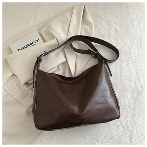 Détail d'un sac hobo en similicuir marron foncé avec bandoulière sur un tissu à carreaux
