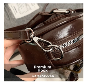Détail du fermoir mousqueton argenté et de la bandoulière de sac en cuir marron brillant