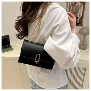 Shoulder shot of black leather flap bag with gold oval buckle and fine chain strap