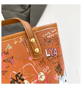 Détail du sac cabas à graffitis avec rivets dorés et texture cuir sur surface marron