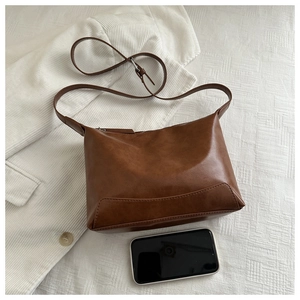 Brown leather tote bag detail with adjustable strap and phone for size comparison