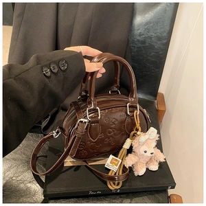 Détail du sac Boston rétro marron foncé avec motifs gaufrés et breloque ours rose