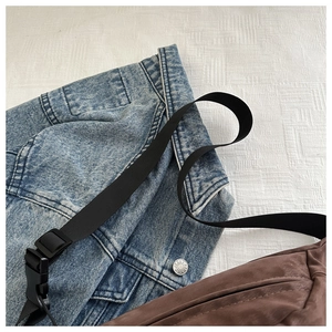 Detail of a brown leather waist bag with black nylon strap on blue denim jacket