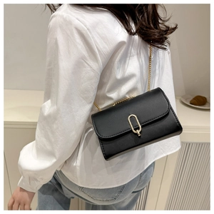 Detail of a chic black faux leather crossbody bag featuring an oval gold metal lock and chain