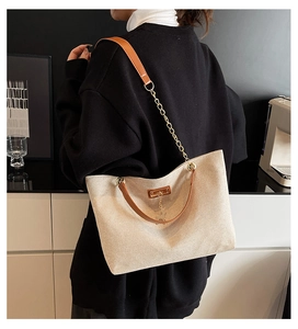 Detail of beige canvas tote bag with brown leather handles and gold chain strap decoration