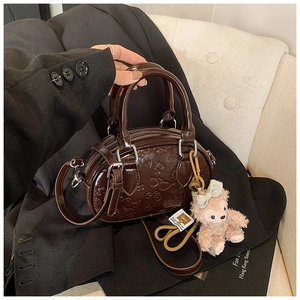 Détail du sac Boston en similicuir marron gaufré avec un gri-gri rose en peluche