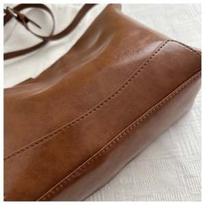Detailed macro view of the double stitching and vintage brown leather texture of this tote bag