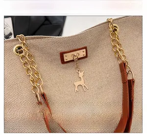Detail of beige woven tote bag with gold hardware, deer charm, and leather strap