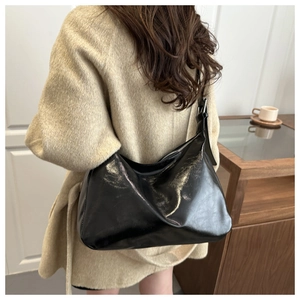 Détail du sac hobo en cuir noir brillant avec boucle métallique argentée sur bandoulière