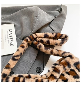 Flat lay of leopard print faux fur shoulder bag next to an artistic book and gray coat