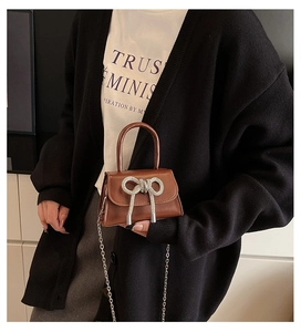 Détail macro du mini sac marron en cuir PU avec nœud strass brillant et bandoulière chaîne métal