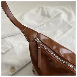 Detail of silver zipper and reinforced stitching on a brown leather shoulder bag