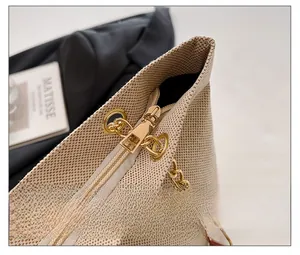 Close-up of beige woven texture bag with gold zipper and metallic chain strap detail