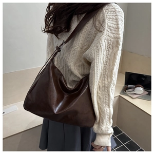 Détail d'un grand sac fourre-tout en cuir marron avec bandoulière porté par un modèle