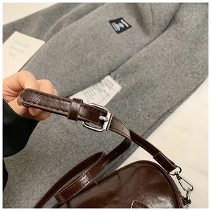 Détail d'une bandoulière en cuir marron foncé avec boucle et trous en métal argenté