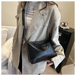 Detail view of a minimalist black square crossbody bag with silver zipper on a model