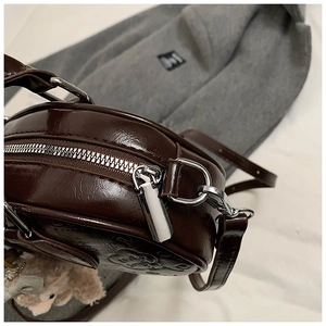 Gros plan du sac à bandoulière marron foncé avec fermeture éclair et breloque peluche