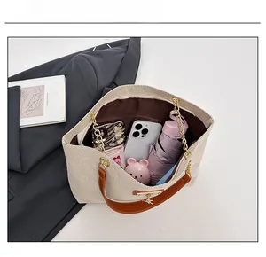 Detailed interior of a beige woven tote bag with brown leather handles and gold chains