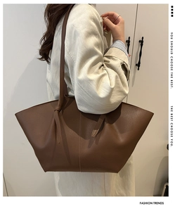Close-up of brown pebbled leather tote bag side wings on model in beige trench coat