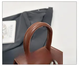 Détail de la poignée en cuir marron avec couture nette et strass sur le mini sac à main