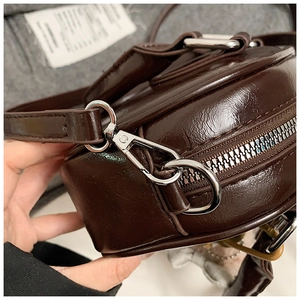 Détail des crochets argentés et de la texture en cuir ciré brillant du mini sac marron