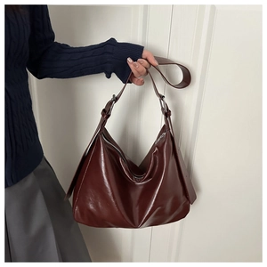 Détail du sac hobo en cuir verni bordeaux avec boucle argentée et large bandoulière