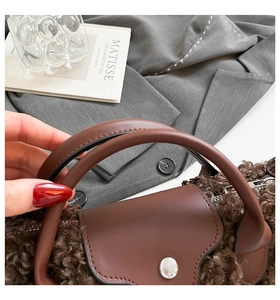 Detailed close-up of brown faux shearling handbag with smooth leather handle and metal button
