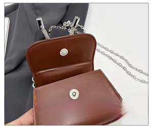 Détail du fermoir magnétique argenté sur un mini sac à main en cuir marron avec chaîne