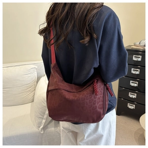 Detail of burgundy leopard print crossbody bag featuring woven red zipper pull accents