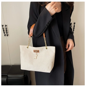 Detail of beige canvas tote bag featuring gold chain strap and deer pendant