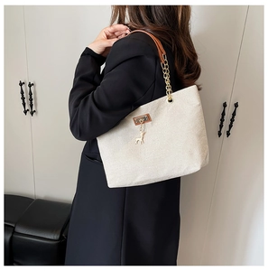 Detail of canvas tote bag with leather chain strap and gold deer charm on shoulder