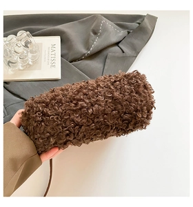 Close-up of a brown faux fur plush bag held by hand against a grey blazer and art book