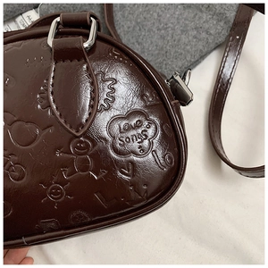Détail macro du sac bandoulière en cuir marron foncé avec motifs gaufrés ludiques