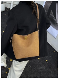 Détail d'un sac hobo en daim marron avec fermoir tournant doré porté sur un blazer noir