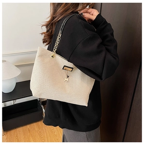 Detail of beige canvas tote with metal chain strap and a golden deer pendant charm