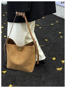 Gros plan d'un sac seau en daim marron avec fermoir doré sur feuilles de ginkgo