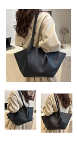 Close-up of black pebble grain leather tote bag showing knotted strap detail on coat