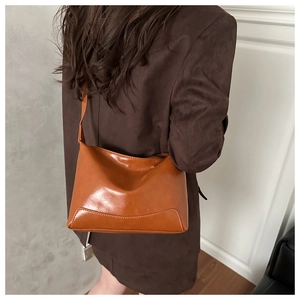 Side view of model wearing the orange-brown glossy leather shoulder bag with sleek stitching