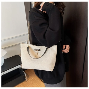 Detail view of the cream woven shoulder bag with black strap and golden deer charm