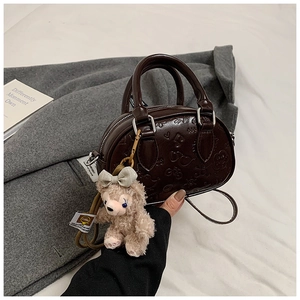 Détail du sac Boston marron foncé avec gaufrage, breloque ours en peluche et motifs cœur