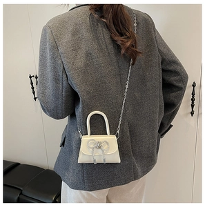 Mini sac crème avec nœud porté en bandoulière dans un décor moderne minimaliste