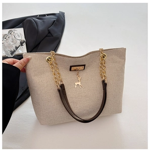 Close-up of beige woven tote bag featuring gold chain strap and elk metal pendant