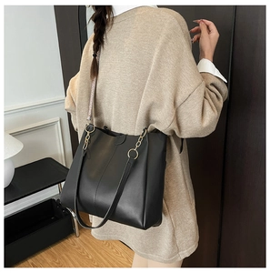 Detail of a large black tote bag with gold chain strap on a model in a modern interior