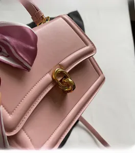Detail of pink leather handbag with gold metal clasp and floral scarf wrapped on handle