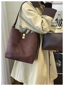 Détail du sac seau en daim marron avec fermoir doré et pochette assortie sur un trench