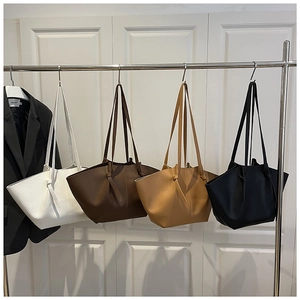 Detail of four minimalist tote bags in textured leather hanging on a metal display rack