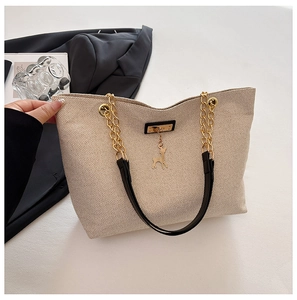 Detail of beige woven tote bag with gold chain strap and elegant deer charm pendant