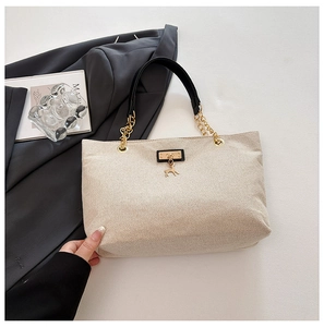Detail of beige woven tote bag with gold deer pendant and elegant black leather handle