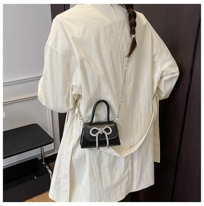 Vue arrière du mannequin portant un mini sac noir avec nœud en strass et chaîne